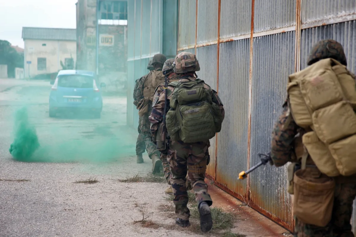 Des légionnaires et des Marines progressent ensemble près d’un bâtiment pendant un exercice.